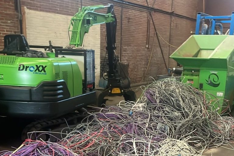 Kabelrecycling Groene machine naast een berg gesloopte kabels in een grote, lege ruimte.